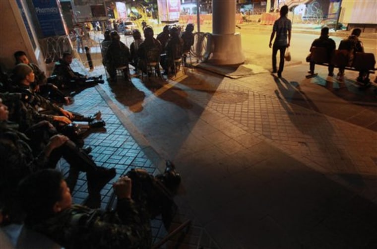 A Thai man carries home dinner as he passes by closed shops and Thai soldiers at an empty bus stop Friday in Bangkok. 